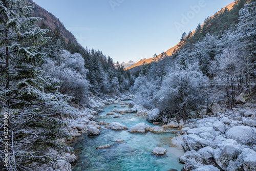 panoramica su un bellissimo ambiente naturale nel fondovalle tra le montagne della Slovenia con vista sul fiume Isonzo, circondato da sponde piene di alberi ghiacciati, di giorno in inverno photo