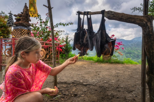 A young girl admires hanging giant bats against a beautiful Balinese backdrop, showcasing culture and nature, Bali, Indonesia photo