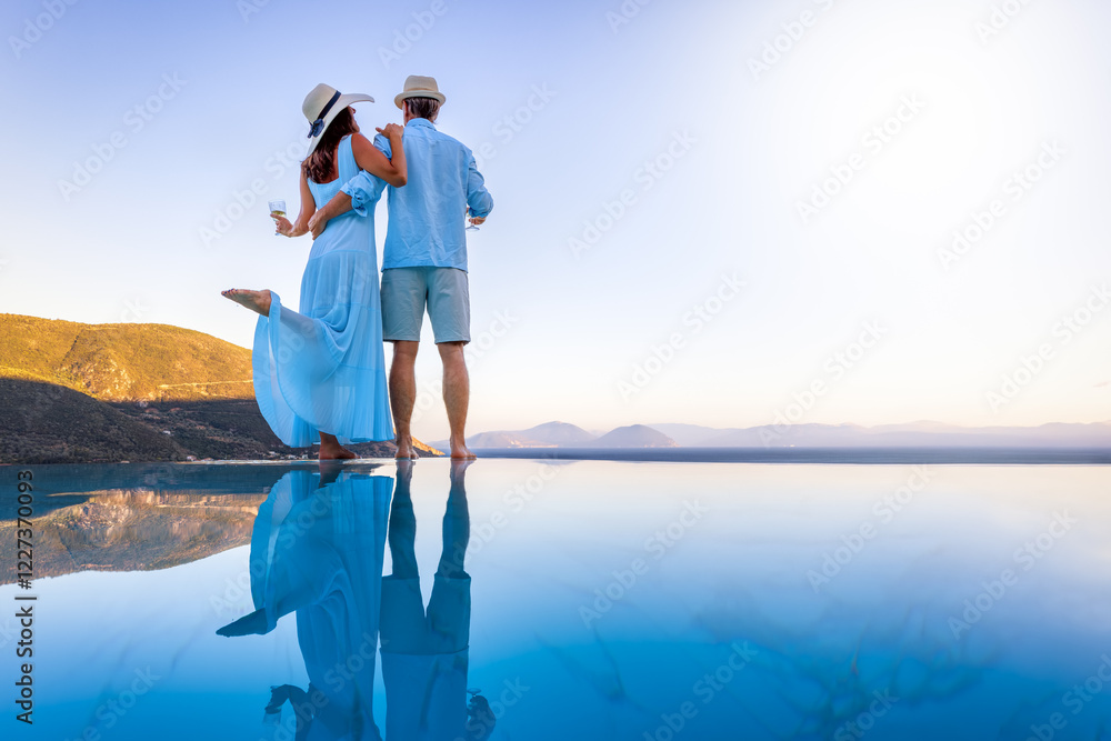 A elegant summer vacation or honeymoon couple enjoys the mediterranean sunset with a glass of wine by the pool