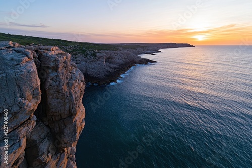 A breathtaking view of the ocean from rocky cliffs at dusk, embodying serenity and solitude as the sun sets, enveloping the land in cooler tones of the evening sky. photo