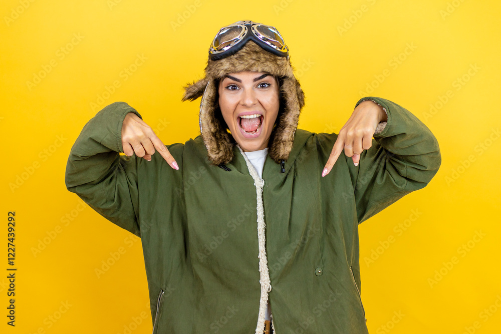 Fototapeta premium Young beautiful aviator woman wearing vintage pilot helmet with glasses and jacket over yellow background looking confident with smile on face, pointing oneself with fingers proud and happy.