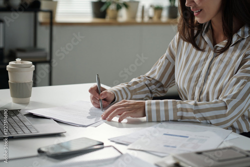 Cropped shot of smiling young female economist signing business contract after reading its main terms photo