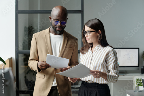 Young serious businessman and brunette woman looking through financial documents while discussing papers