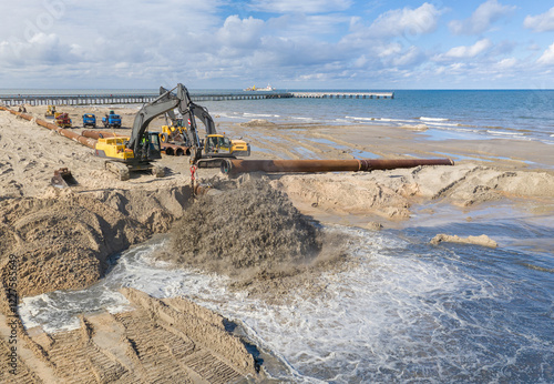 Beach restoration sand Bulldozers. Mud flows from the pipe with excavator behind for the reconstruction of the beach taken away by the sea. Work in progress for beach nourishment. Drone shot. photo