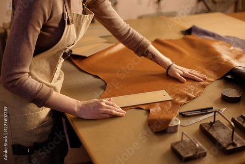 Hands cutting leather on workbench with precision, surrounded by tools, suggesting craftsmanship in process of creating handmade leather goods photo