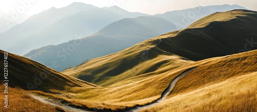 Mountaineering path winding through golden hills with serene mountain backdrop and space for text addition