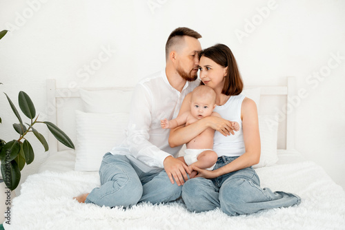 mom, dad with a baby, an international family, a Caucasian mom with an Asian husband and a baby in her arms in the bedroom gently hugs the baby holding in her arms, a place for text photo