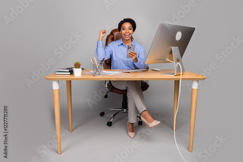 Confident businesswoman sitting at desk celebrating success while checking phone in a modern office setting photo