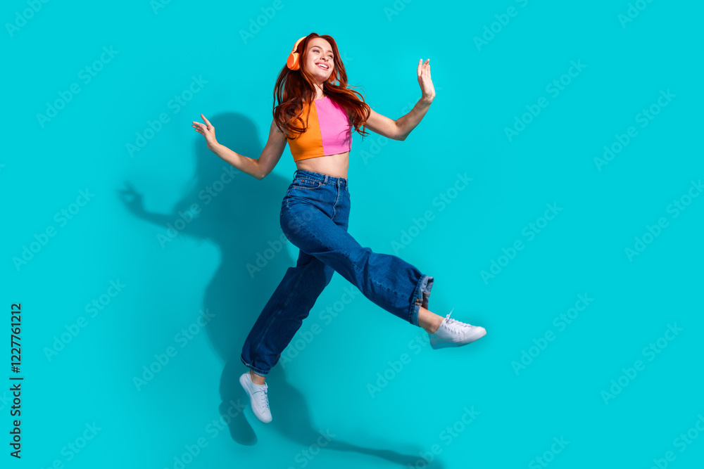 Obraz premium Joyful young woman in summer casual outfit and flared jeans jumps against teal background