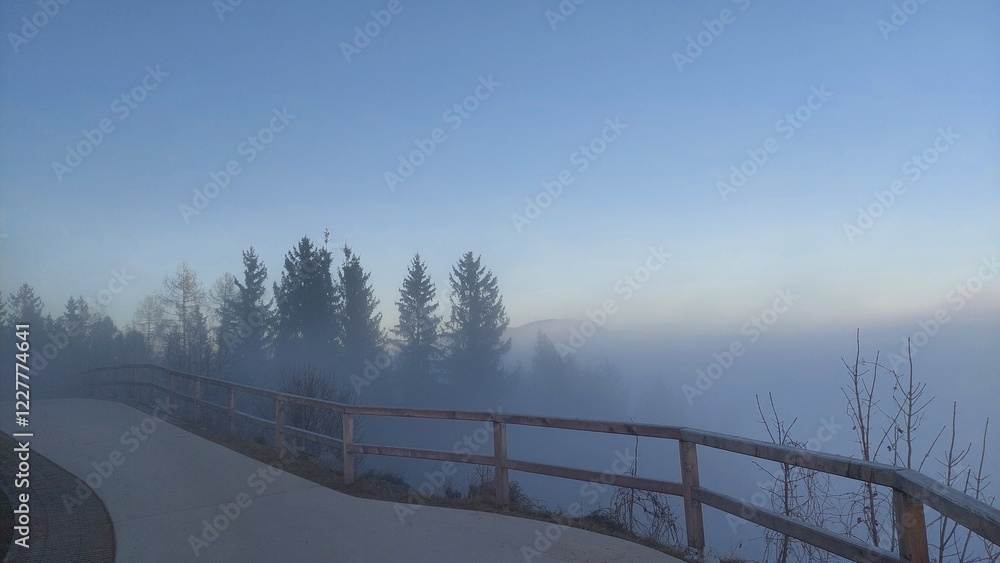 Fototapeta premium Observation deck on the hillside overlooking the valley. Silhouettes of trees in the fog