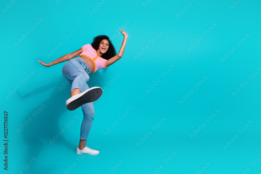 Fototapeta premium Cheerful young woman joyfully posing against a vibrant turquoise background