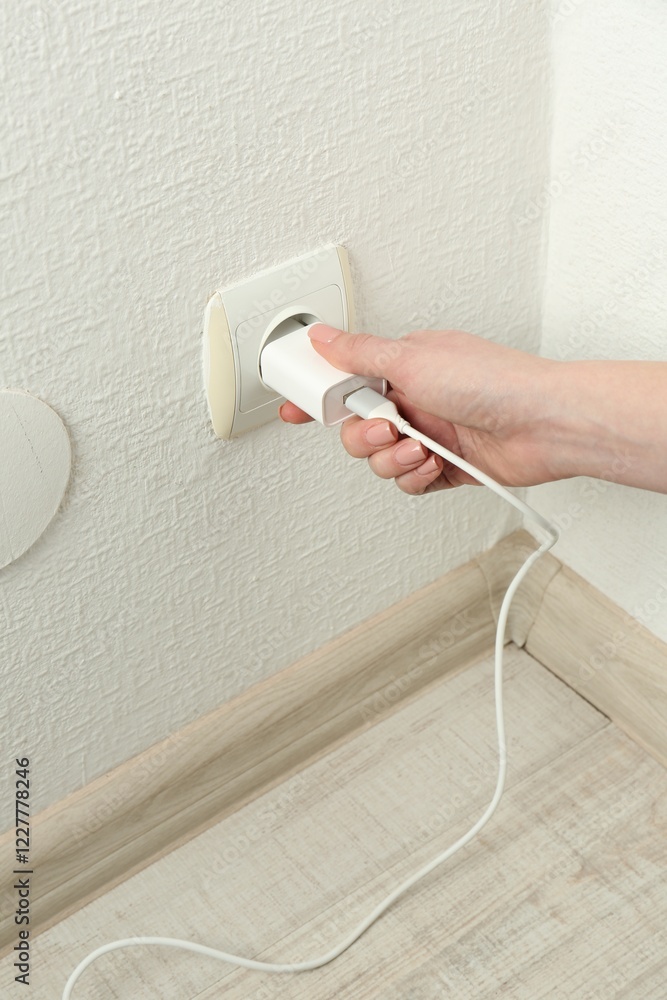 Fototapeta premium Woman plugging USB power adapter with charge cable into electrical socket indoors, closeup