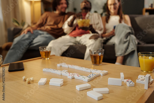 Domino tiles and three glasses of juice standing on wooden table against group of happy young friends photo