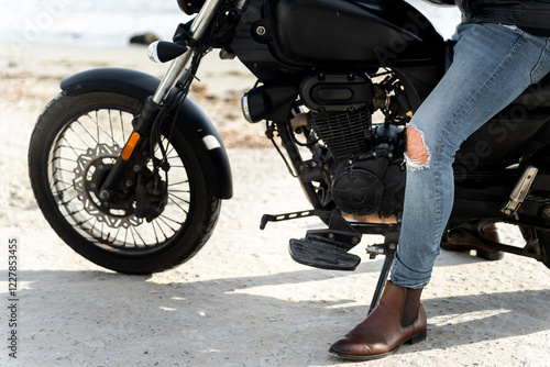 Biker wearing ripped jeans and chelsea boots sitting on a motorcycle on the beach