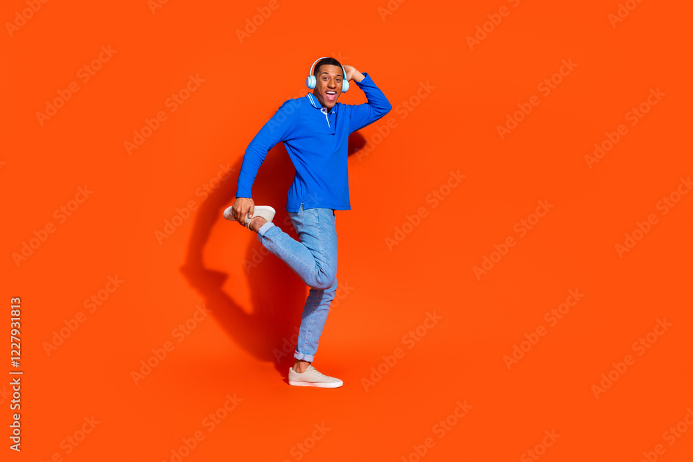 Joyful young man in blue polo poses against vibrant orange background Joyful young man in blue polo poses against vibrant orange background