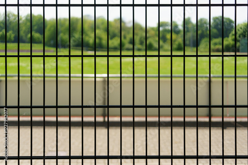 A metal fence in front of a green football pitch at a small local stadium in Germany.