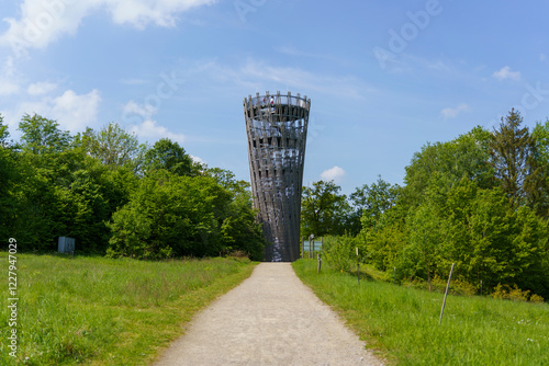 A wooden and metal tower in Hemer, Germany, standing in Sauerland Park during summer, with a blue cloudy sky in the background.