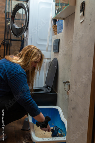 Cleaning a litter box in a laundry room during the evening