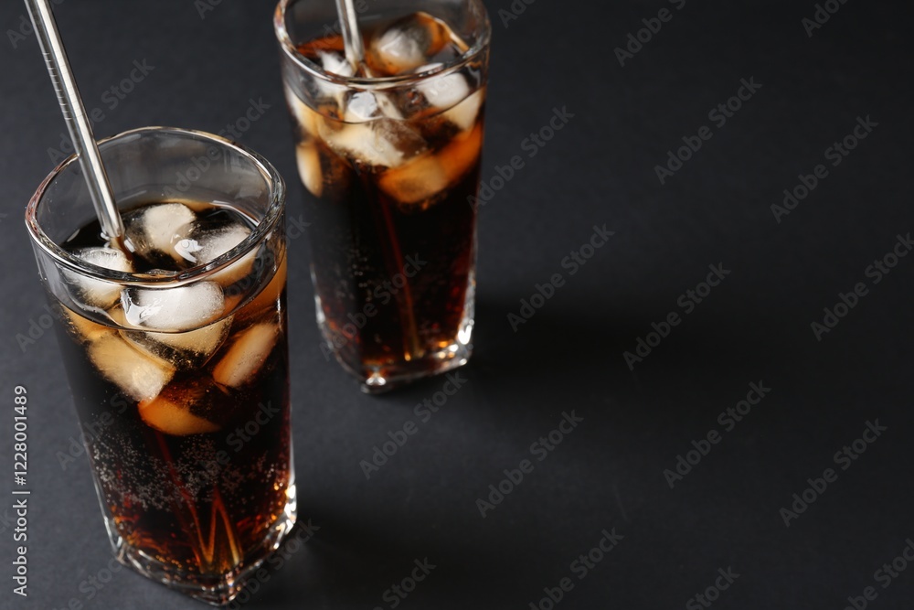 Refreshing cola with ice cubes and drinking straws in glasses on black table, closeup. Space for text Refreshing cola with ice cubes and drinking straws in glasses on black table, closeup. Space for text