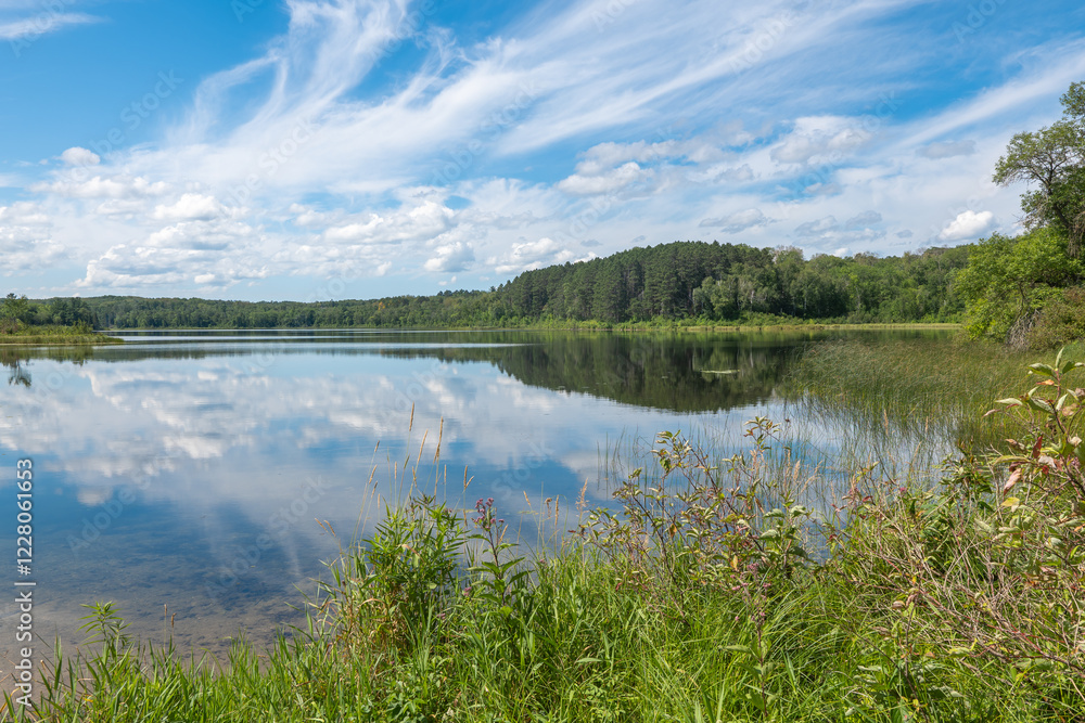 Idyllic landscape of calm water and reflection of blue sky and clouds at the shore of a Minnesota lake.