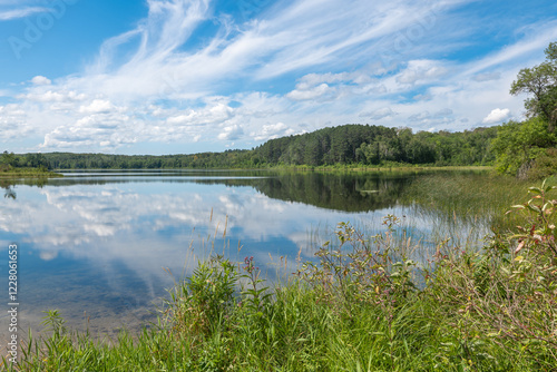Obraz na płótnie Idyllic landscape of calm water and reflection of blue sky and clouds at the shore of a Minnesota lake. w salonie