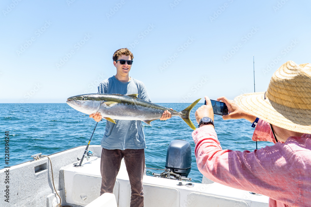 A young man smiling proudly as he holds up his freshly caught fish, posing for a photo to capture the memorable fishing moment.