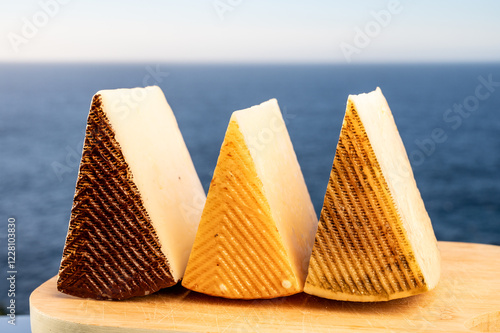 Assortment of Spanish hard cheeses, curado, manchego, goat cheese served outdoor with blue sea on background, close up photo