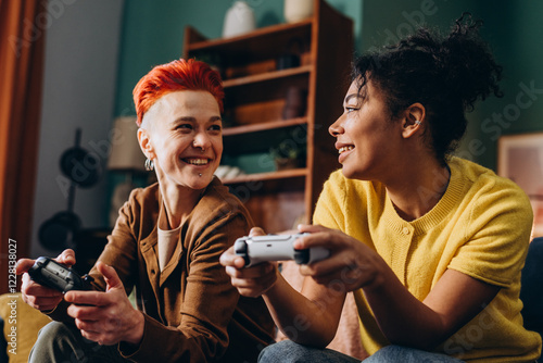 Smiling lesbians with joysticks enjoy video games sitting on sofa at home
