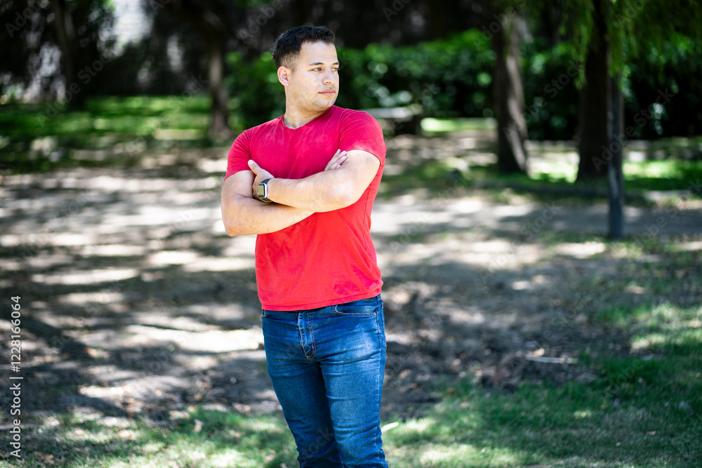 Latin man with arms crossed in a park with a serious expression