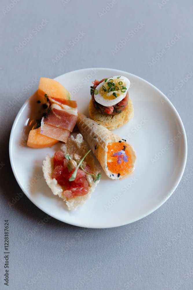 Elegant assortment of gourmet appetizers on a white plate served at a modern dining venue during an evening gathering Elegant assortment of gourmet appetizers on a white plate served at a modern dining venue during an evening gathering