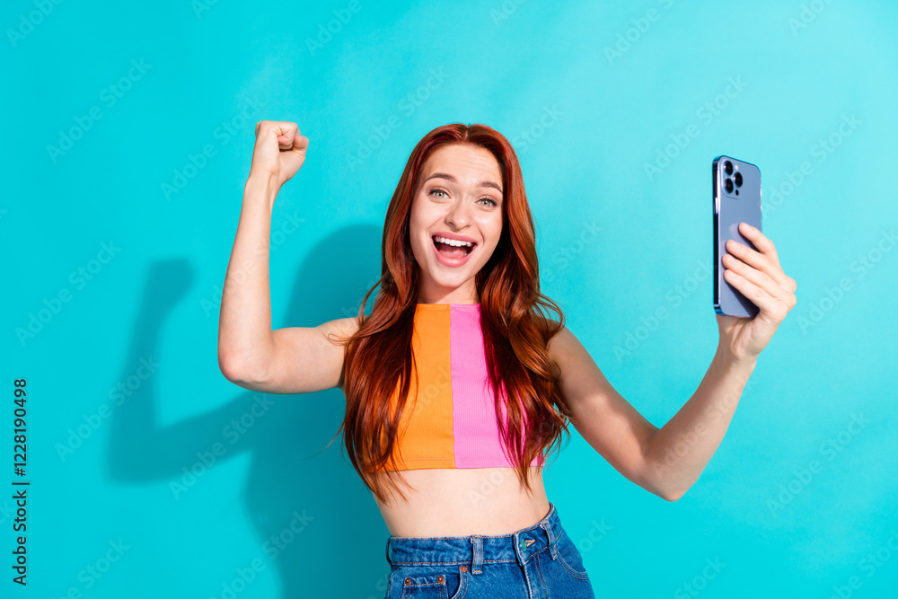 Excited young woman with red hair taking a selfie against teal background in summer casual outfit Excited young woman with red hair taking a selfie against teal background in summer casual outfit