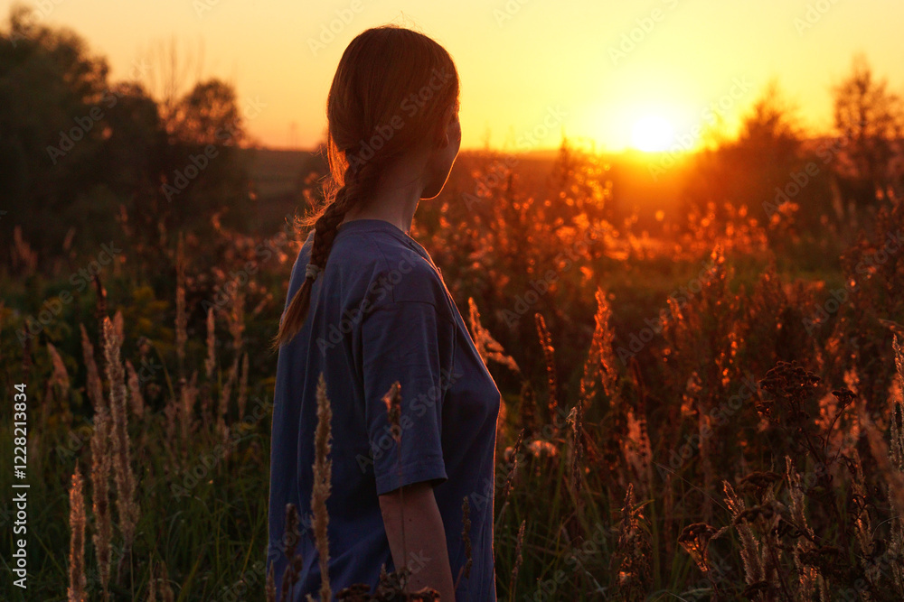 A young woman stands in a sunlit field surrounded by plants during sunset. A young woman stands in a sunlit field surrounded by plants during sunset.