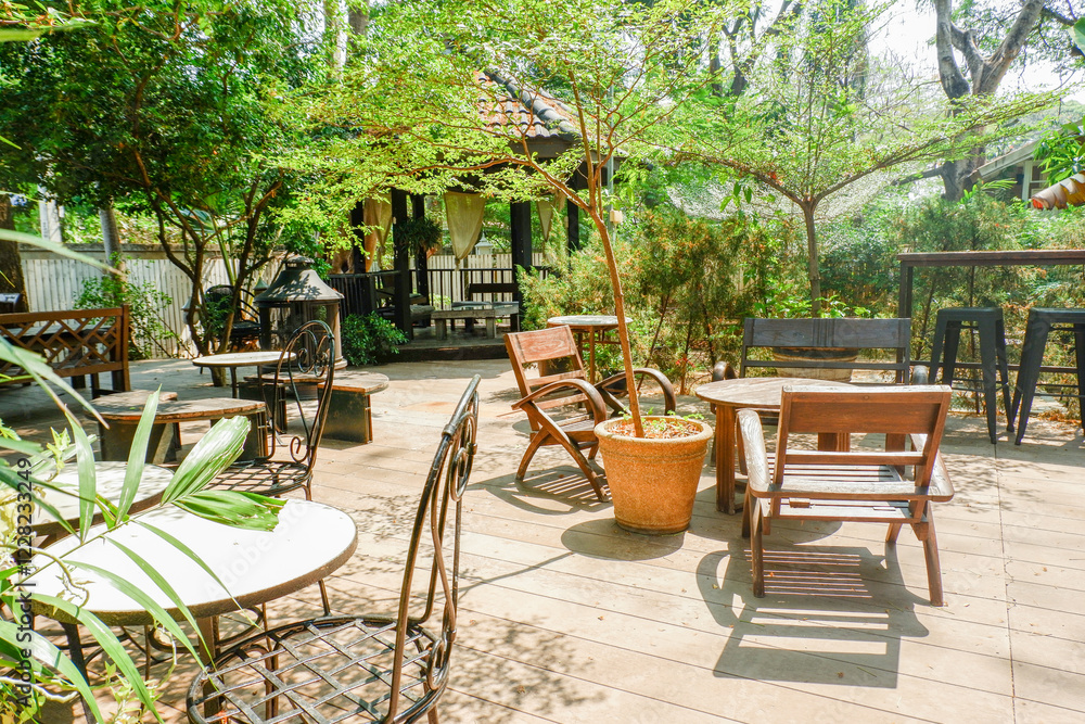 Wooden table and chair set in garden on a sunny day,outdoor seating for restaurant or cafe,Neat paved patio with sitting area and small garden in forest. Wooden table and chair set in garden on a sunny day,outdoor seating for restaurant or cafe,Neat paved patio with sitting area and small garden in forest.