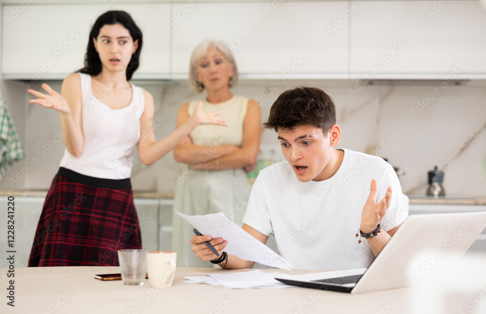 Young student guy does homework on laptop and swears with elderly mother and young girl sister. Conflict, quarrel, violation of personal boundaries Young student guy does homework on laptop and swears with elderly mother and young girl sister. Conflict, quarrel, violation of personal boundaries