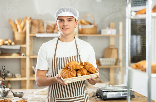 Smiling young man demonstrating croissants in right-angled woven basket in bakehouse photo