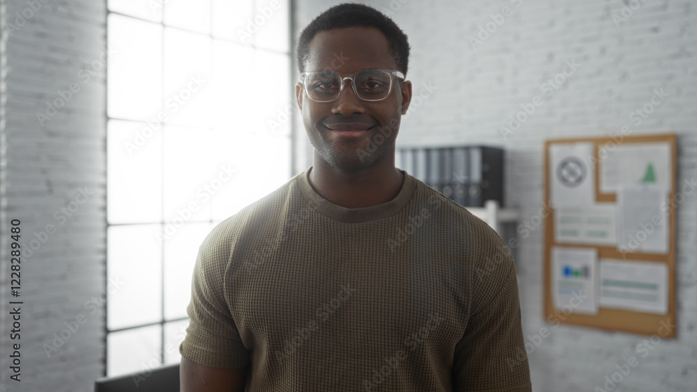Obraz premium Young man standing confidently in a modern office environment, showcasing a professional and approachable demeanor, with documents on a bulletin board in the background.