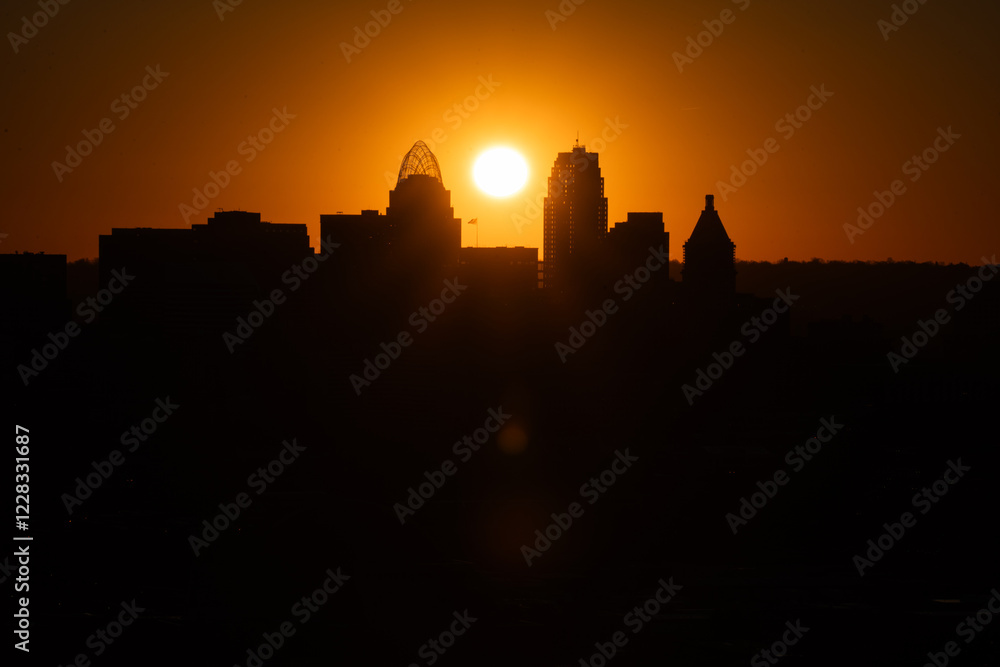 Fototapeta premium Sunrise over Cincinnati downtown city skyline with silhouettes of buildings and warm orange hues