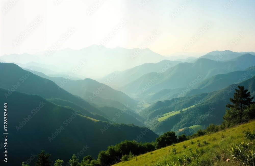 Fototapeta premium Vast mountain range stretches across horizon. Rich green plants and valleys are visible within mountain range. Gentle hills descend towards valley. Misty atmosphere adds to serene beauty of landscape.