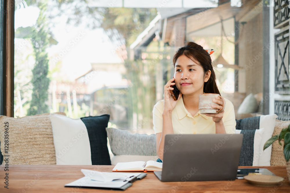 A young woman multitasks with a laptop and coffee while on a phone call, enjoying a bright and cozy home environment. A young woman multitasks with a laptop and coffee while on a phone call, enjoying a bright and cozy home environment.