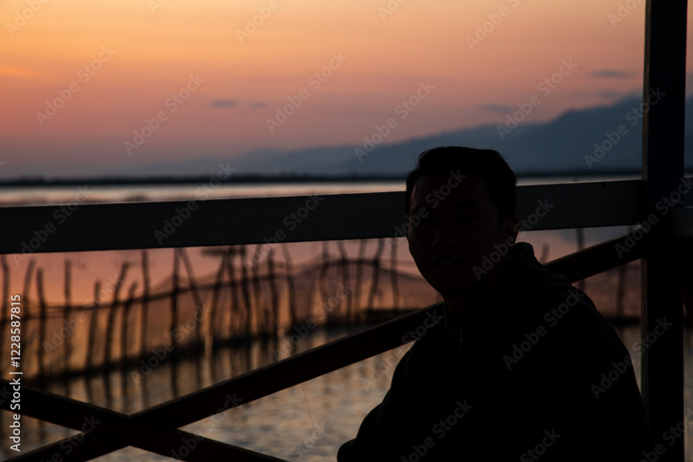 Fototapeta premium Silhouette of a man sitting at the gate enjoying the beautiful sunset on the beach