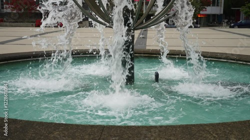 Water flows at high speed and pressure out of a water feature fountain from multiple points in a public square in Vancouver splashing into the bowl below filled with clear, clean water photo