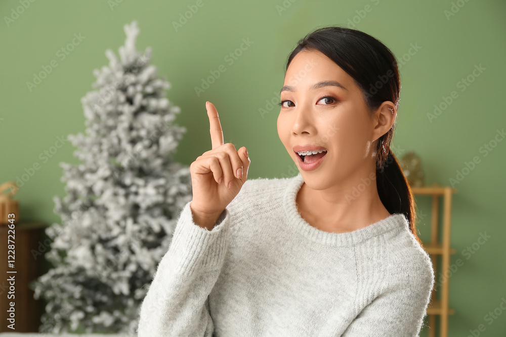 Portrait of pretty young Asian woman pointing at something in living room with Christmas tree Portrait of pretty young Asian woman pointing at something in living room with Christmas tree