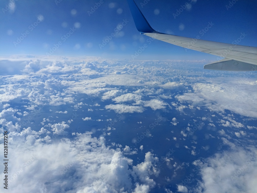Fototapeta premium view from airplane window reflecting white clouds and glowing sea