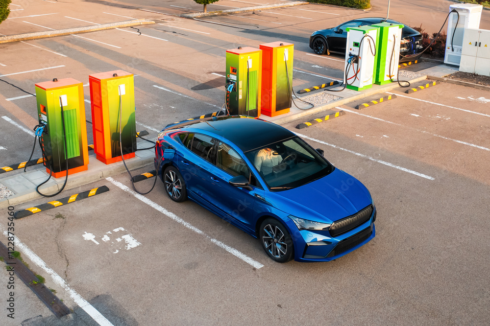 Modern vehicle receives electricity at public charging point. Parking lot equipped with plugs and connectors for quick replenishing of energy