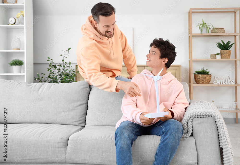Teenage boy with wind turbine model and his father sitting on sofa at home Teenage boy with wind turbine model and his father sitting on sofa at home