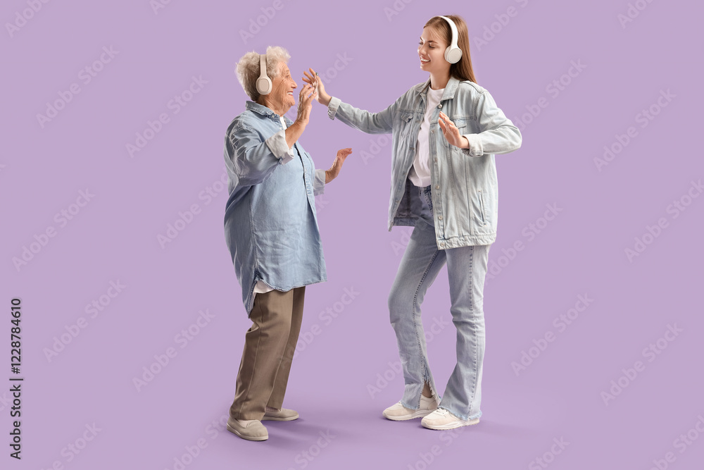 Naklejka premium Happy senior woman and her granddaughter in headphones dancing on purple background