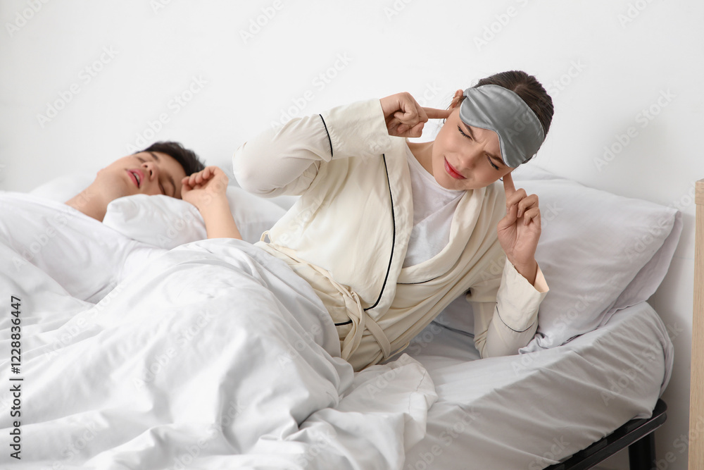 Obraz premium Young irritated woman lying in bed with her snoring husband at home
