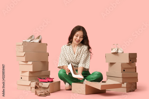 Quadro su tela Young Asian woman with high heel and shoe boxes sitting on pink background
