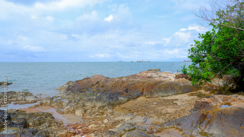 A serene beach view with a rocky shore with a little greenery and clear blue skies and fluffy white clouds. A serene beach view with a rocky shore with a little greenery and clear blue skies and fluffy white clouds.