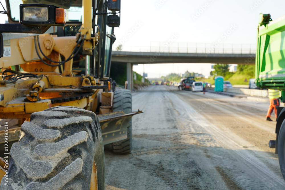 Fototapeta premium Road construction machine leveling and smoothing the gravel base to create a stable foundation for new asphalt paving